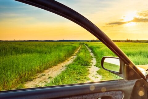 Car door open to a scenic dirt road through green fields at sunset in Portland, OR