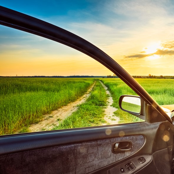 Car door open to a scenic dirt road through green fields at sunset in Portland, OR